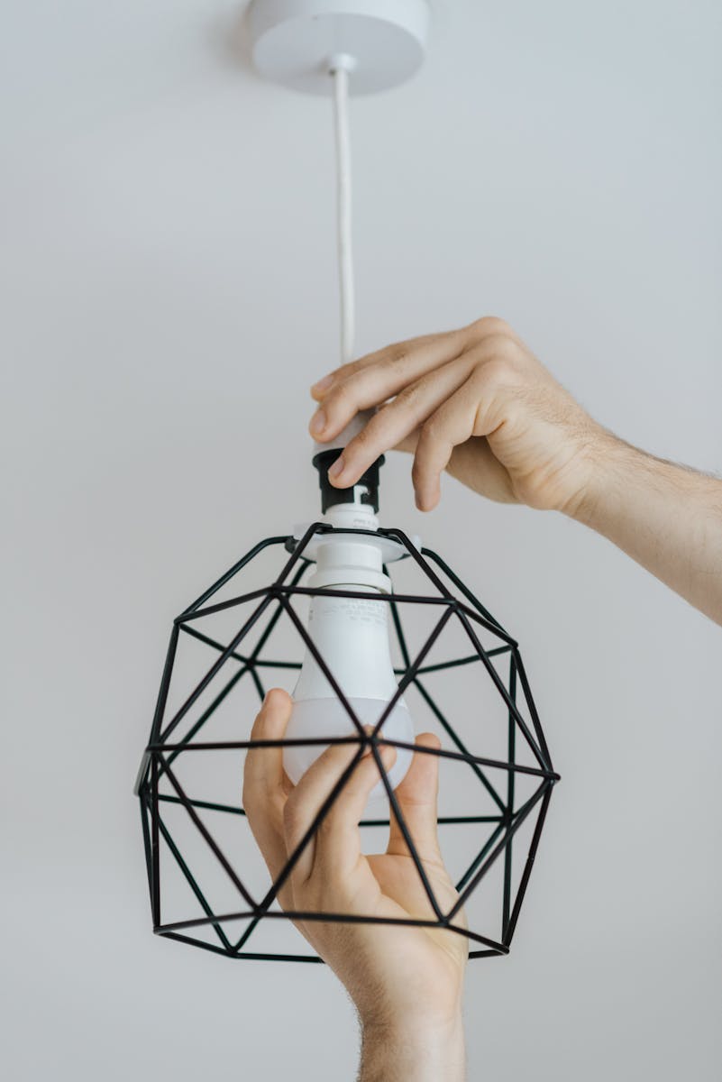 Close-up of hands installing a light bulb in a contemporary geometric wire lamp indoors.